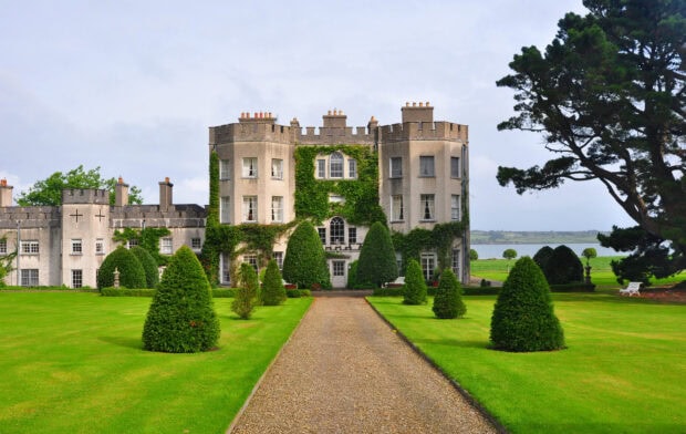 A grand Irish castle surrounded by lush green gardens and manicured trees