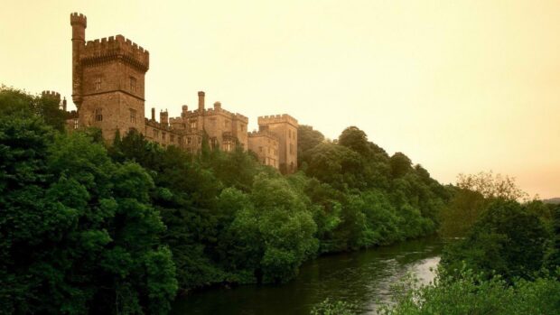 Ancient Irish castle surrounded by lush greenery and a flowing river at sunset