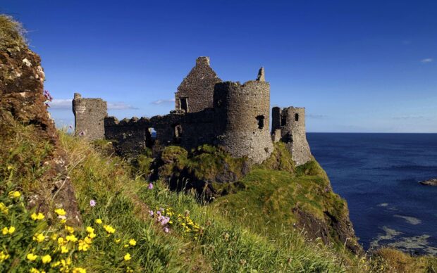 Ancient Irish castle ruins on cliff with green grass and ocean view