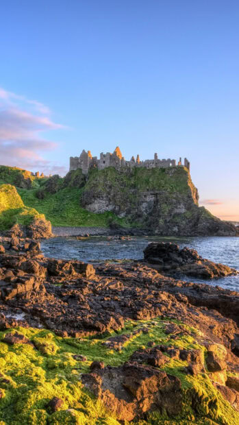 Ancient Irish Castle ruins on rocky coastline with green moss and clear sky