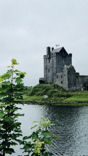 Historic Irish castle surrounded by water and greenery on a cloudy day