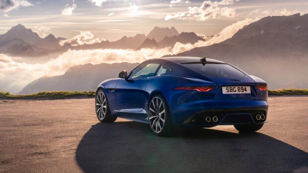 Blue Jaguar Cars parked on a mountain road with scenic clouds and peaks in the background