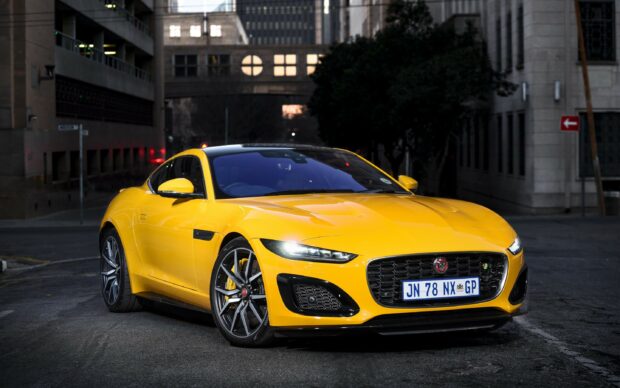 Bright yellow Jaguar car parked on city street at dusk with glowing headlights