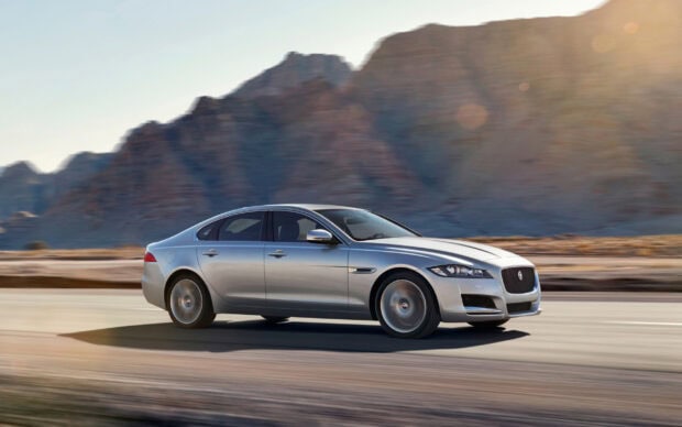 Silver Jaguar car driving fast on desert road with mountain background