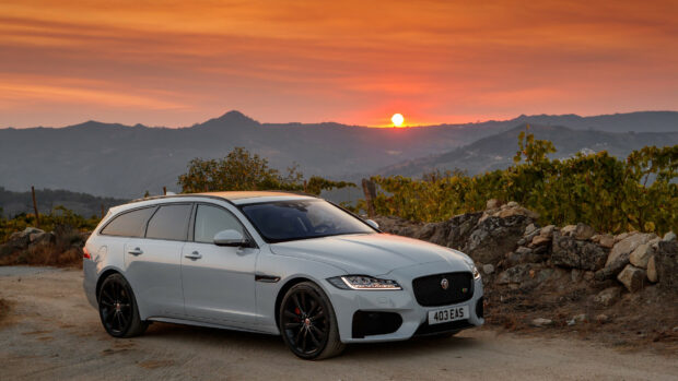 White Jaguar car parked on dirt road with mountain sunset background
