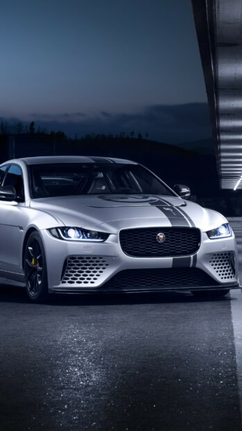 A sleek Jaguar car parked under a modern structure at night with illuminated headlights
