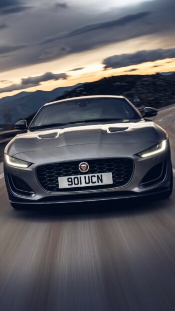 A sleek Jaguar car driving fast on a mountain road during sunset