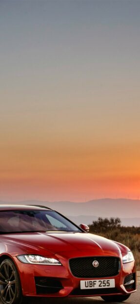 Red Jaguar car driving at sunset with mountains in the background