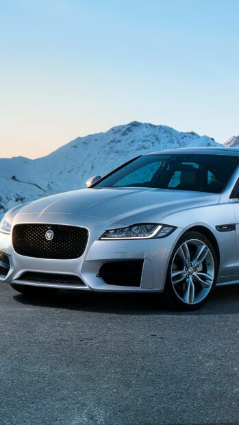 A silver Jaguar car parked on a mountain road with snow covered peaks in the background