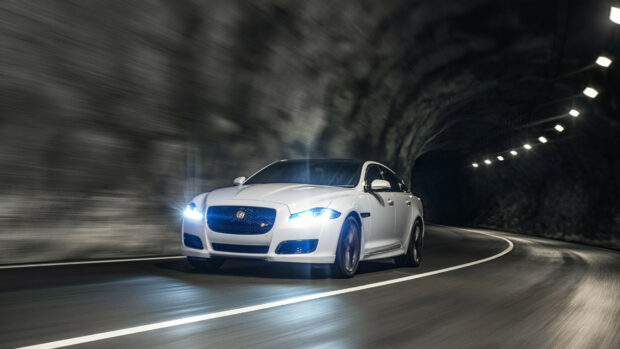 White Jaguar car driving fast inside a tunnel with bright headlights on
