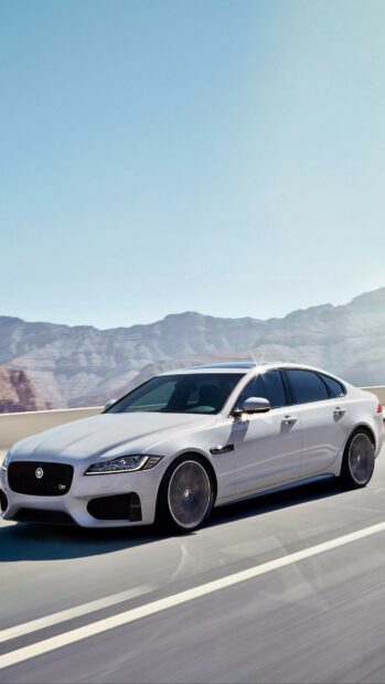 A white Jaguar car driving fast on a highway surrounded by mountains and clear sky