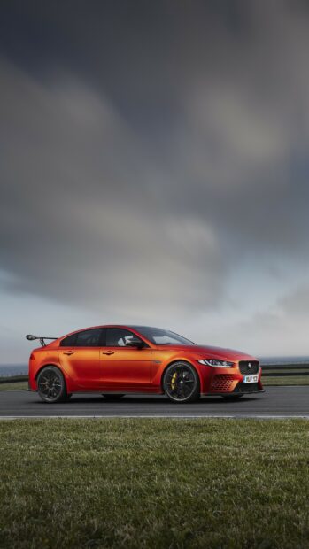 A sleek orange Jaguar car parked on a track with a cloudy sky in the background