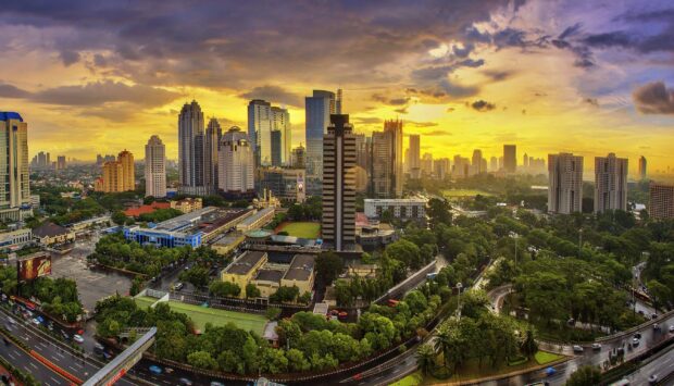 A panoramic view of Jakarta skyline during sunset with skyscrapers and lush greenery in the foreground