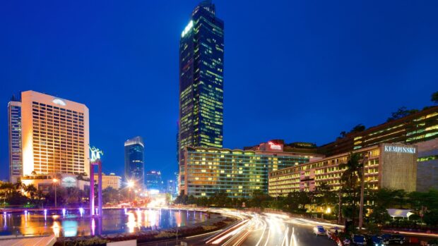 Night view of Jakarta cityscape with modern buildings and light trails around the fountain
