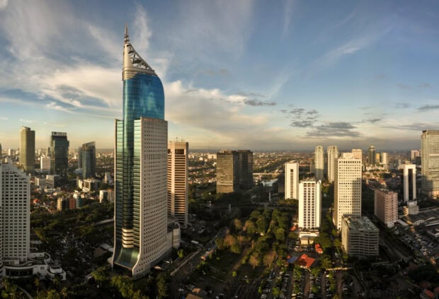 Modern skyscraper in Jakarta cityscape during sunset with clear sky and urban greenery