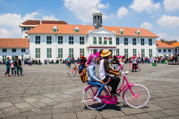 People enjoying a Jakarta city scene with historical building and colorful bicycles