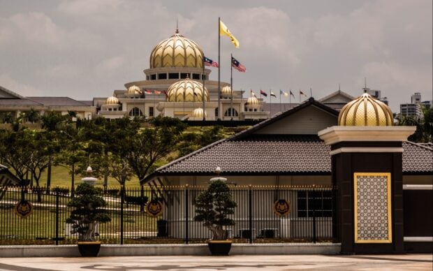 The golden domes of a government building in Jakarta surrounded by lush greenery and flags