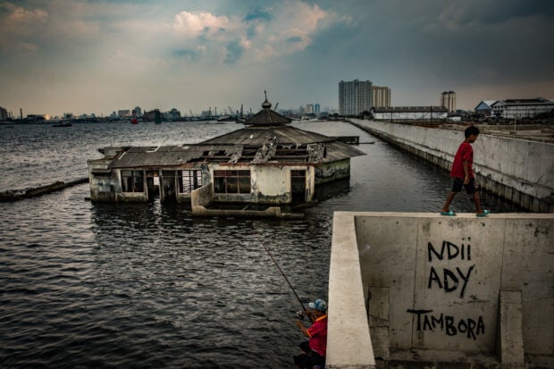 The Jakarta urban landscape with a flooded building and people fishing near the water