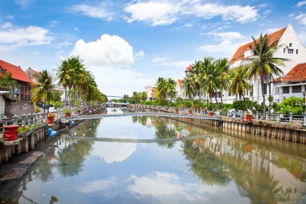 Beautiful canal scene in Jakarta with palm trees and historic buildings under blue sky