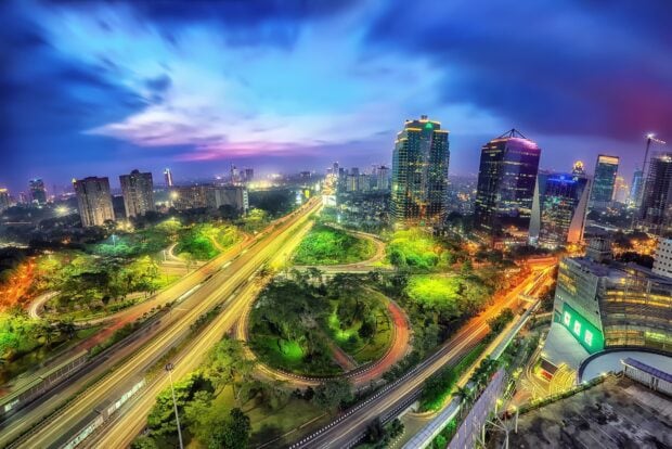 Jakarta cityscape at night with vibrant traffic and green urban areas in the downtown region