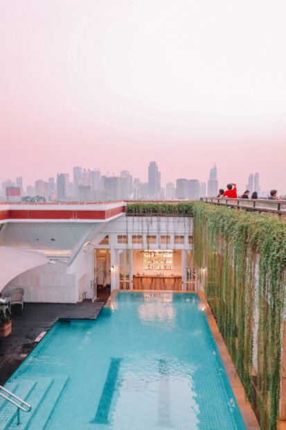 Rooftop pool with hanging plants overlooking jakarta skyline at sunset