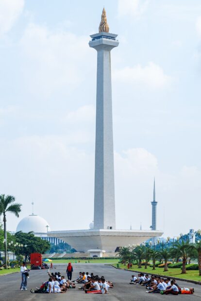 A group of people exercising near the National Monument in Jakarta during a clear day