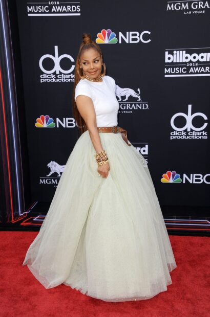 Janet Jackson wearing a white top and flowing skirt standing on a red carpet at a music awards event