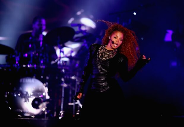 Janet Jackson performing energetically in a live concert setting with a microphone on stage