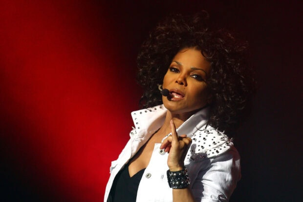 Janet Jackson performing on stage wearing a white studded jacket and headset microphone