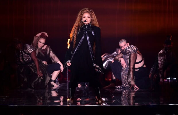 Janet Jackson performing on stage with backup dancers in dark costumes
