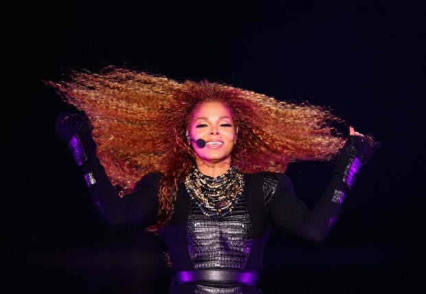Janet Jackson performing on stage with curly hair and black outfit