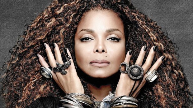 Janet Jackson with curly hair and multiple rings on fingers posing confidently