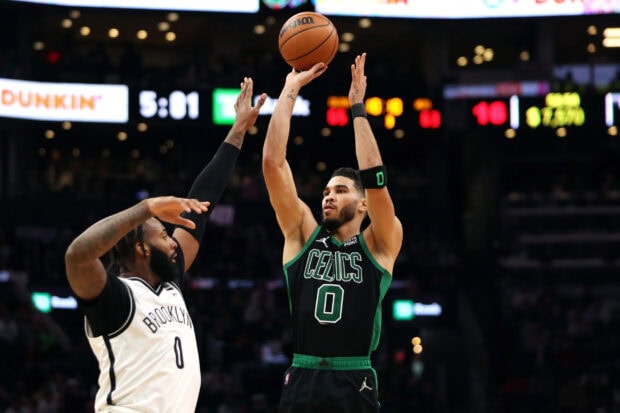 Jayson Tatum shoots a basketball over a defender during a Celtics game in the NBA arena