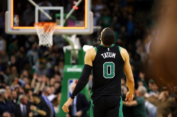 Jayson Tatum walking on the basketball court during an intense game in a packed arena