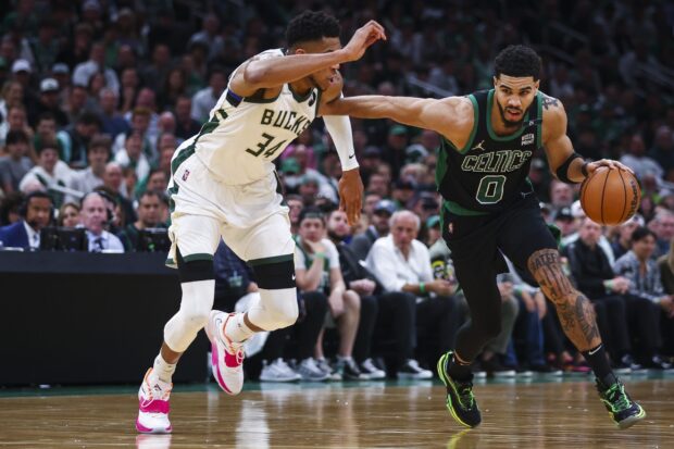 Jayson Tatum dribbling the basketball during an intense NBA game against the Milwaukee Bucks defender