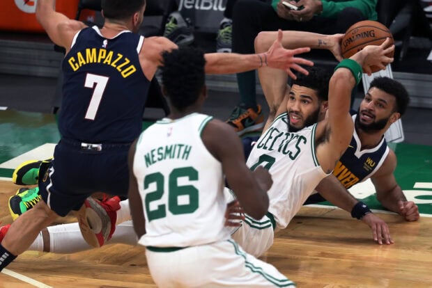 Jayson Tatum holding a basketball on the floor during a basketball game with opponents around
