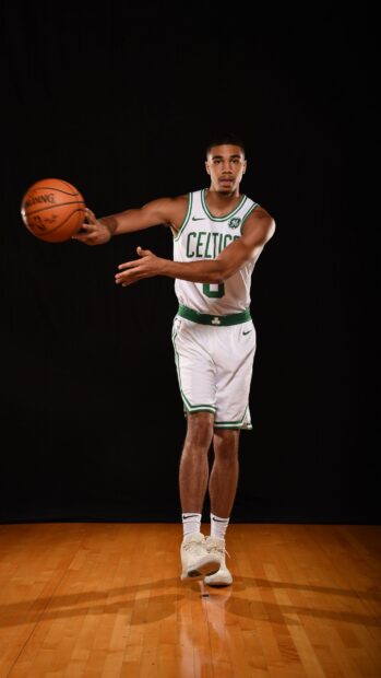 Jayson Tatum in a Celtics uniform passing a basketball on a wooden court