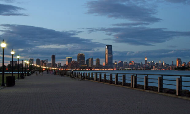 A scenic view of Jersey City skyline at dusk with illuminated street lamps along the waterfront promenade