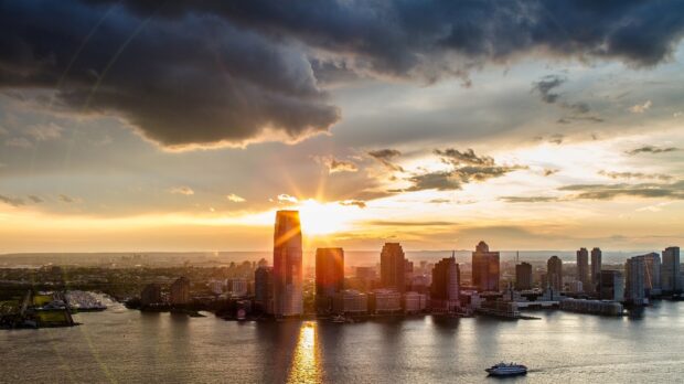 Jersey City skyline with river under dramatic sunset clouds and bright sunlight