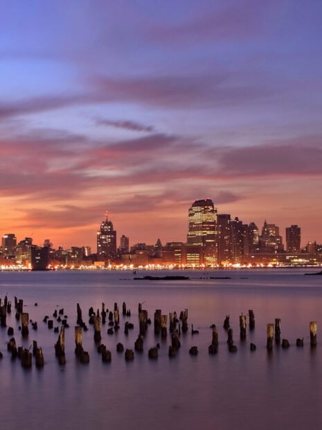 Sunset sky over Jersey City skyline with old wooden posts in water at dusk