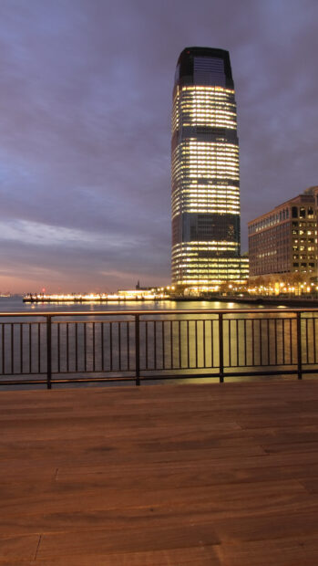 Evening view of Jersey City skyscraper reflecting on the water with wooden deck and railing