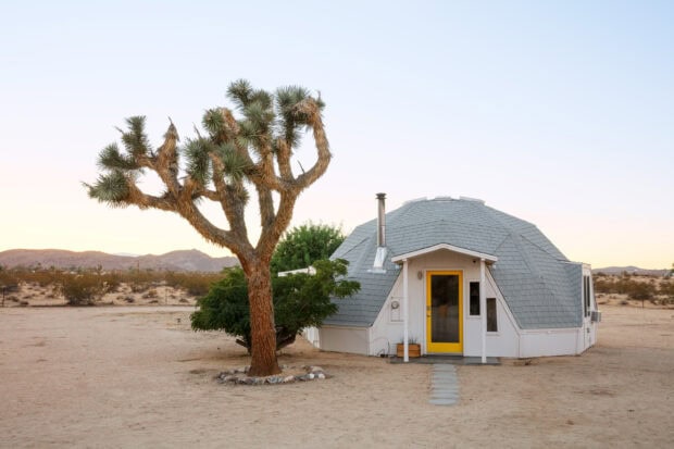 A unique Joshua Tree stands beside a dome shaped house in the desert landscape at sunset