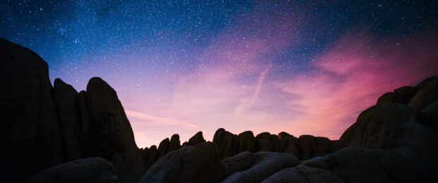 Silhouetted Joshua Tree rocks under a starry sky with purple and blue tones