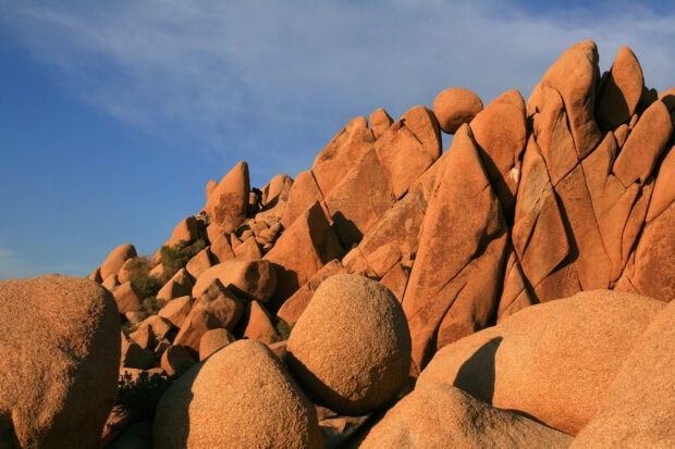 Large natural rock formations at Joshua Tree under clear blue sky with hikers nearby