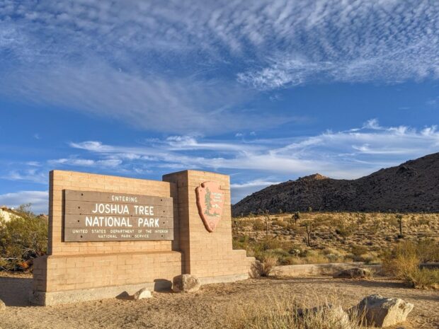 Entering Joshua Tree National Park sign with desert landscape and mountains in the background