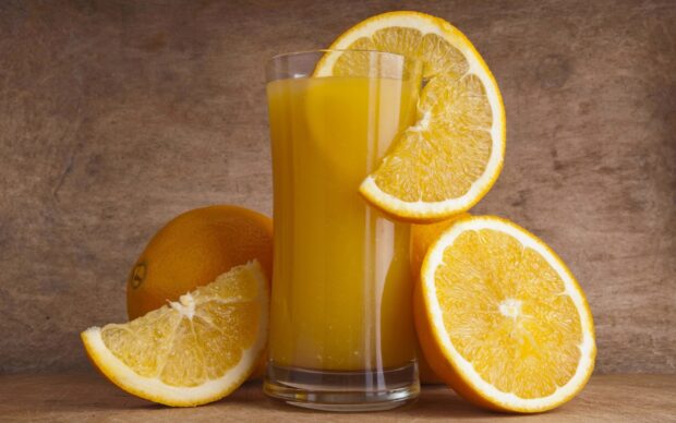 Fresh orange citrus drink surrounded by whole and sliced fruit wedges