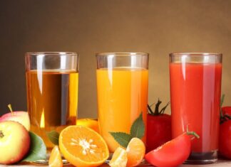 A glass of apple juice orange juice and tomato juice with fresh fruits on a wooden table
