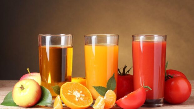 A glass of apple juice orange juice and tomato juice with fresh fruits on a wooden table