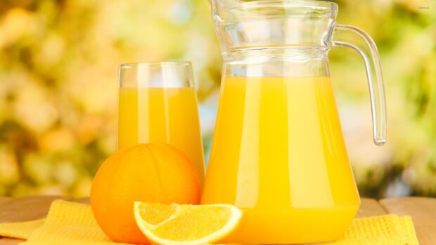 Fresh orange juice with whole and sliced orange on a yellow cloth