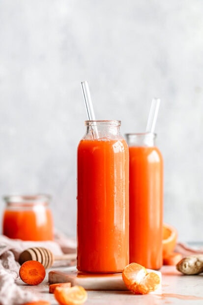 Fresh carrot juice with tangerine pieces and ginger in glass bottles on a table
